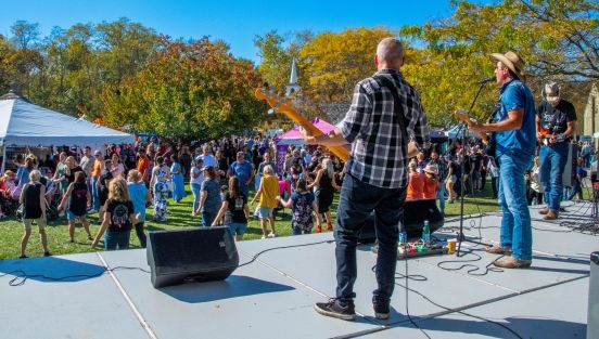 Bandmembers with guitars in hand on stage look out across apple fest crowd