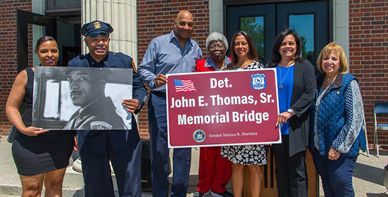 Supervisor Carpenter stands with the children of Det. Thomas as they hold the bridge dedication sign and his photograph