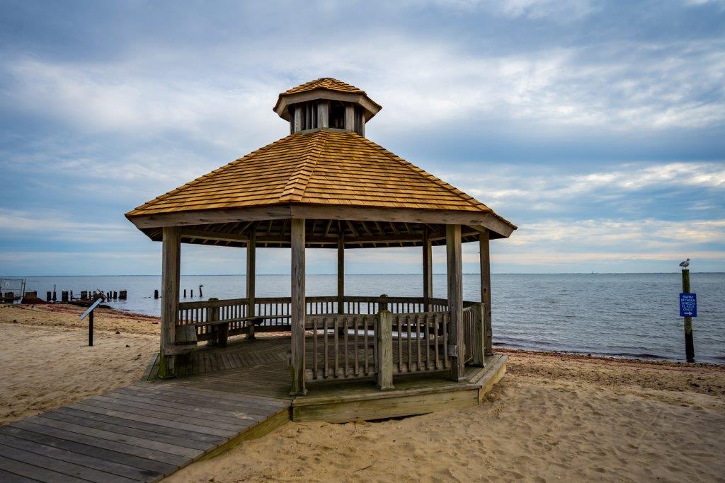 Closer into frame, the gazebo is seen in all it's glory adorner with a crisp new wood shingled roof, through it's awnings the smooth waters rest under a setting sky.