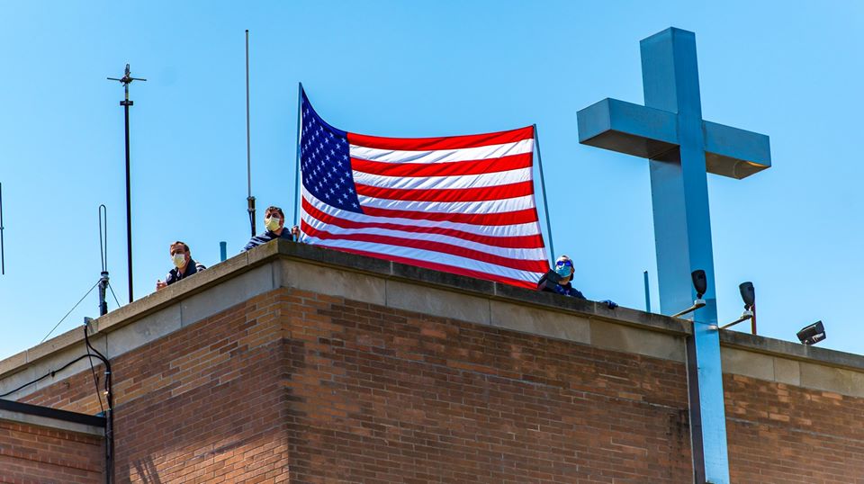 American flag waves ontop of hospital as cross is seen next to it