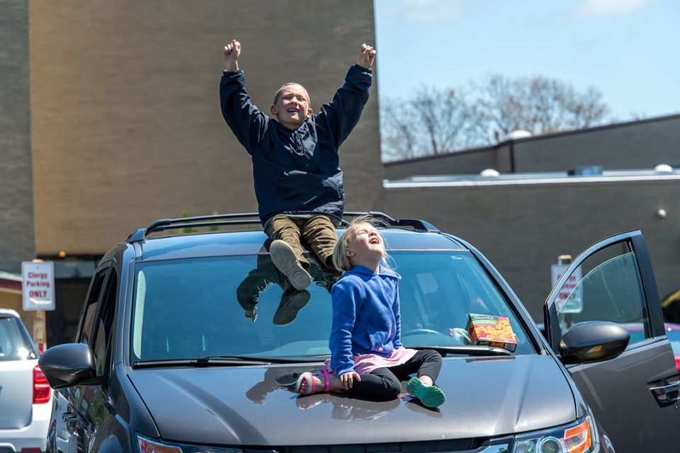 2 children sit on hood on car in awe and excitement of passing flyover