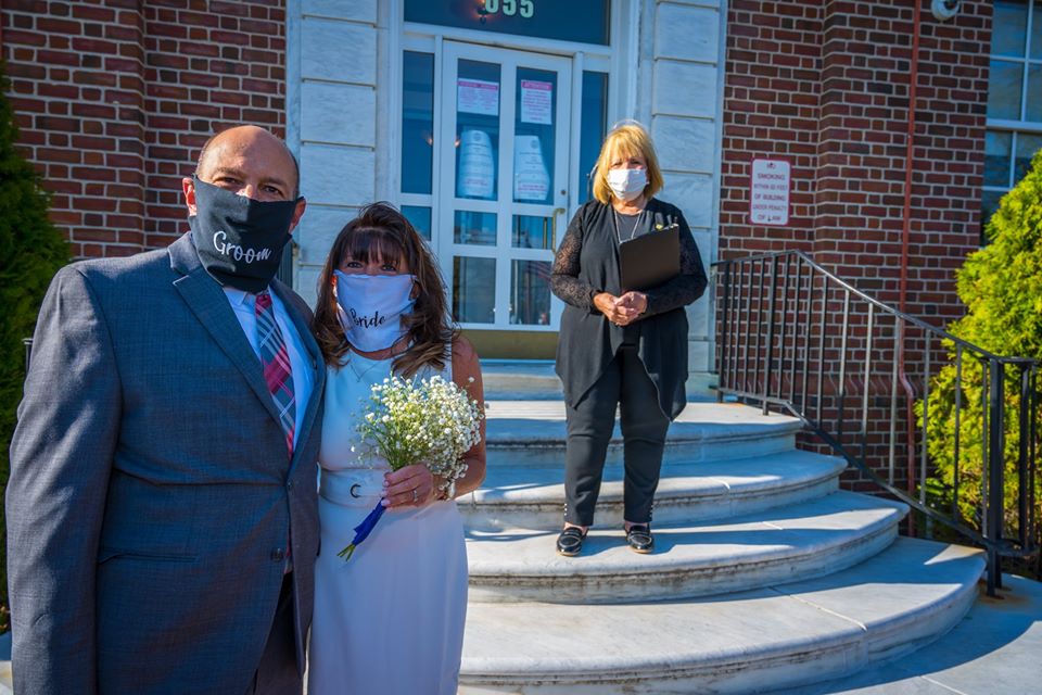 Supervisor Carpenter who officiated the wedding can be seen on the Town Hall steps behind the bride and groom who are in the foreground together with masks on
