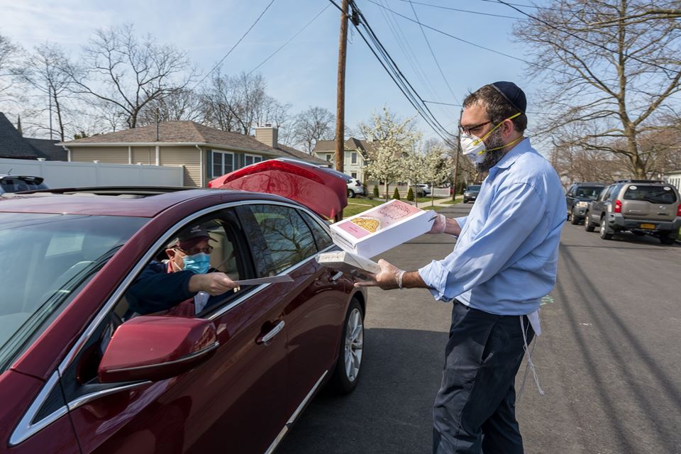 rabbi in mask hands items to person in car in mask