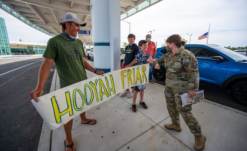 Family of boys with welcome sign, 'elbow bump' returning Commander