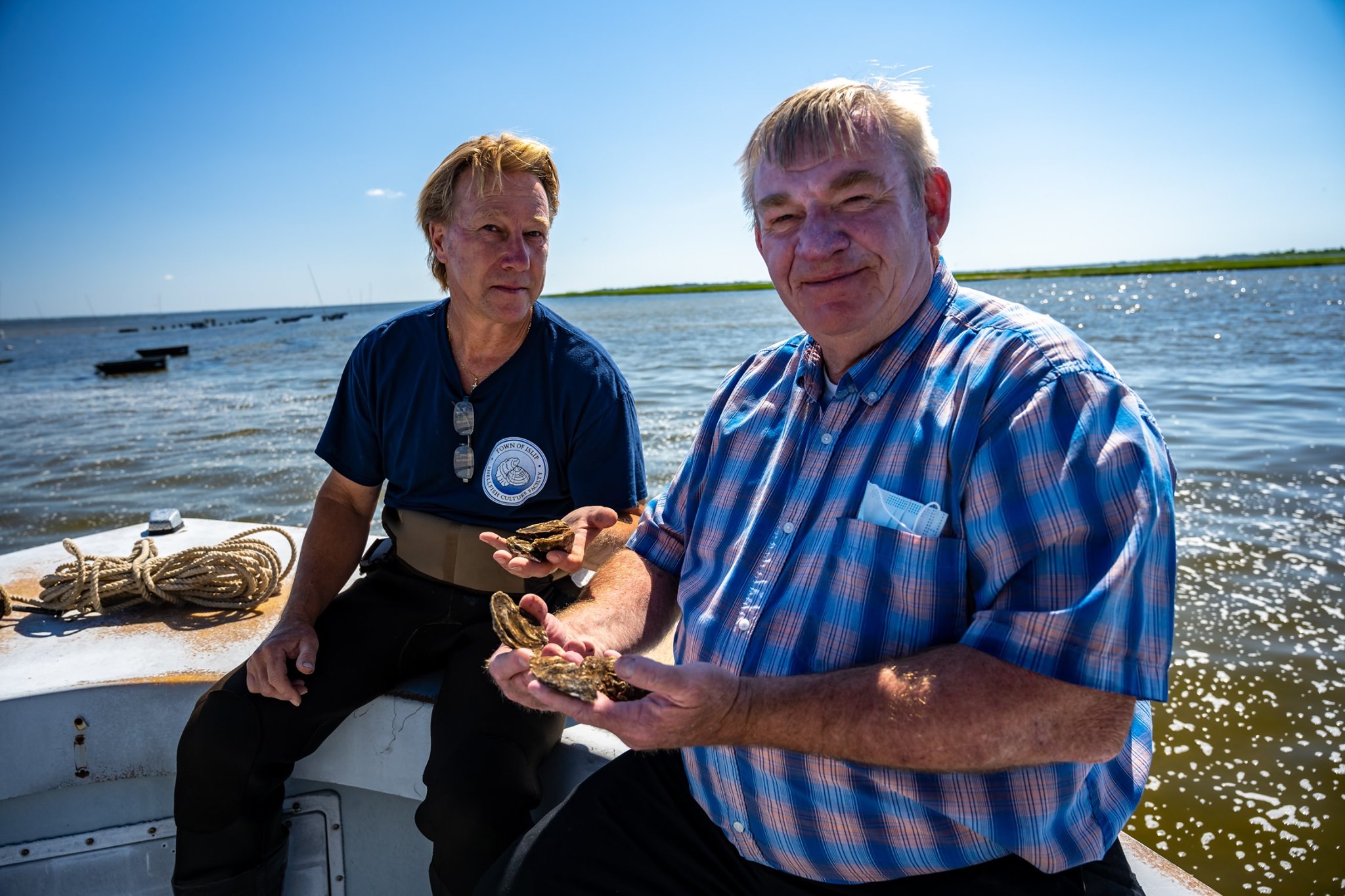 DEC Commissioner Bellew and worker sit on deck with oysters