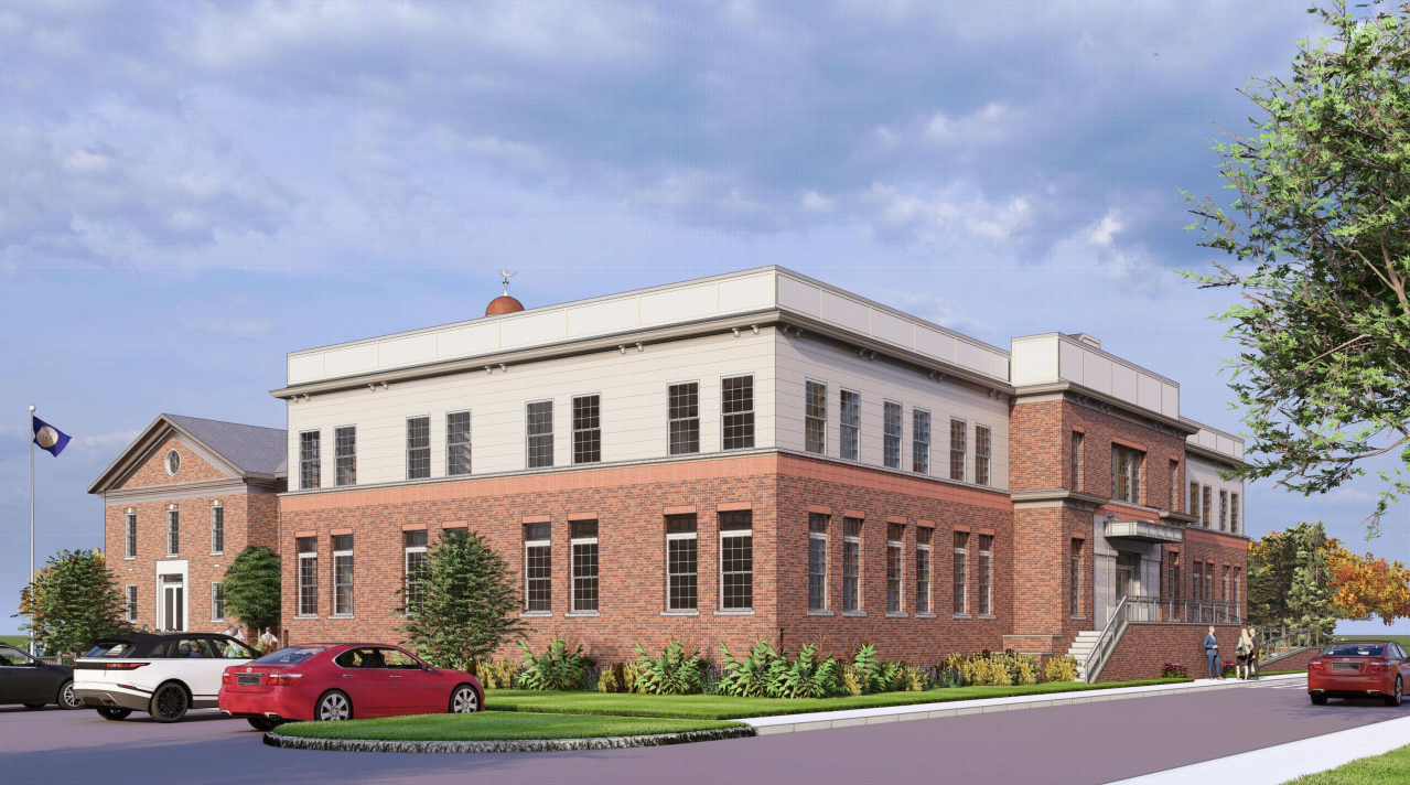 A side angle view of the Town Hall Annex showing its white upper story addition above the brick base, with landscaping and parked cars in the foreground.