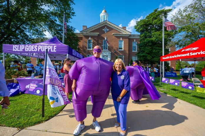 Big inflatable Purple Man in Suit and Purple Mask Poses in front of Town Hall with Angie Carpenter