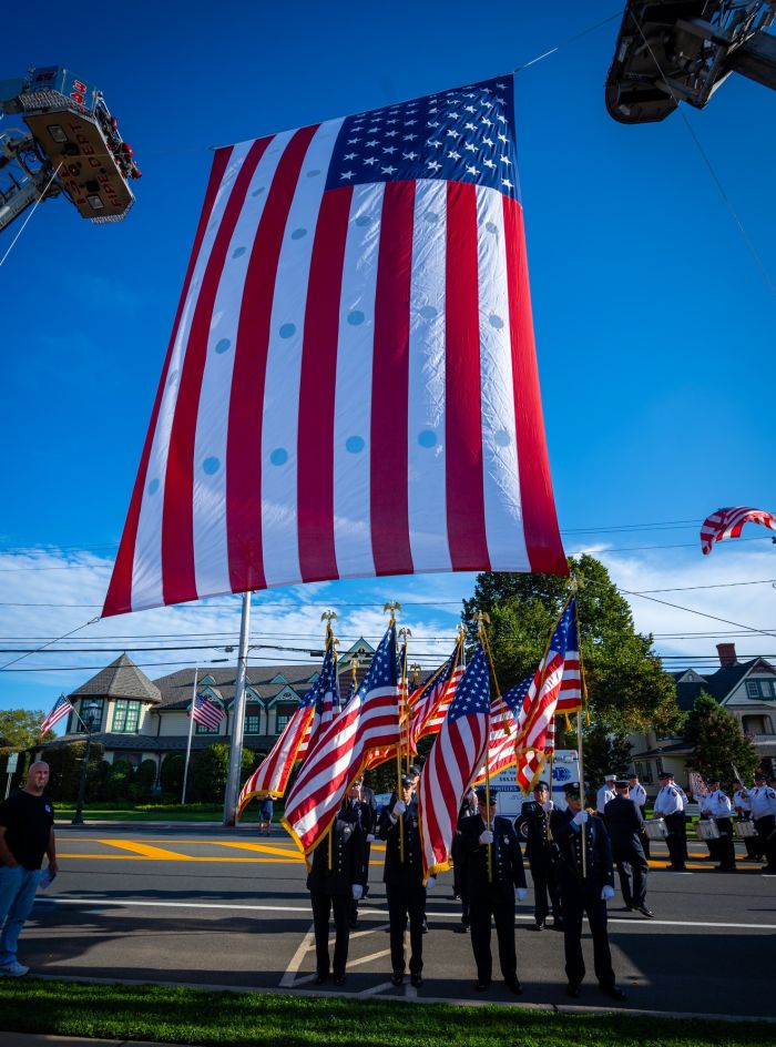 Officers' march with held American Flags as a large flag flows above them, draped between two fire engine ladders