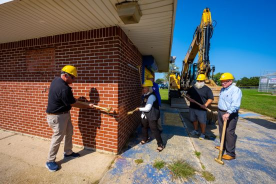 Councilman Cochrane and Supervisor stand at corner of brick structure with golden sledge hammers, mimicking the eventual demolition of the building