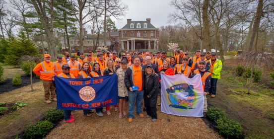 Supervisor Carpenter, Councilwomen Mullen and Bergin along with DPW and Parks Commissioner Owens pose with PSEG Staff and Volunteers on the beautiful grounds of Brookwood Hall holding Town of Islip and Earth Day 2019 flags