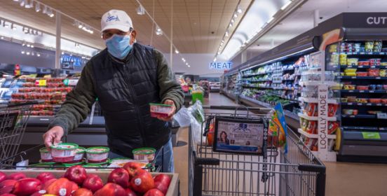 A man in a mask picks apples at the supermarket.