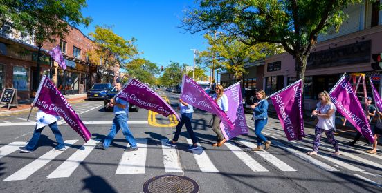 Members of the community wave purple flags walking right to left across Islip Main Street in preparation of the purple event.