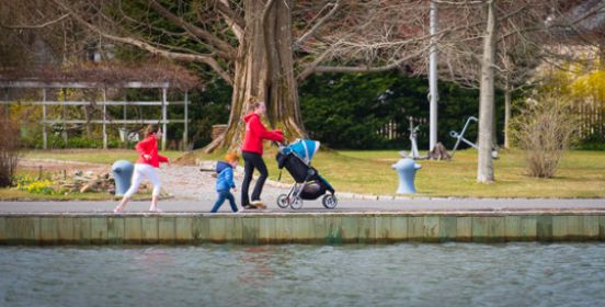 Woman with stroller and children walk along water.