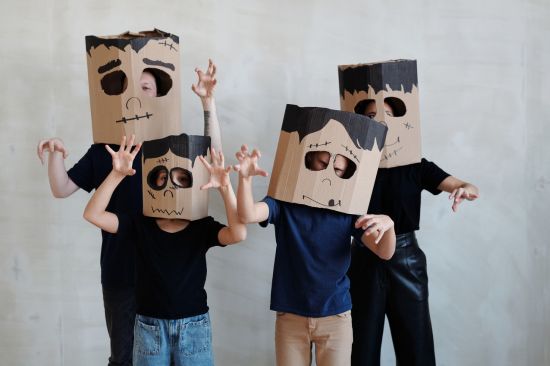 Cardboard boxes colored in black marker in the face of frakenstein ontop of 4 kid's heads as they make a "Scary" pose