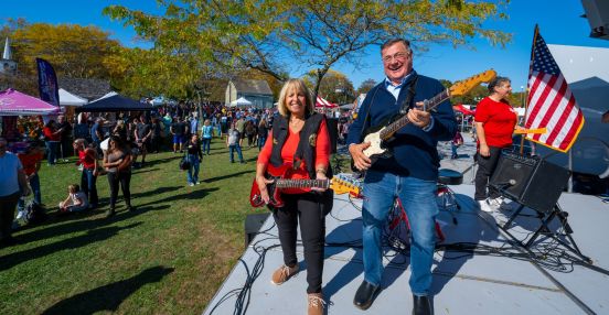 Bandmembers with guitars in hand on stage look out across apple fest crowd