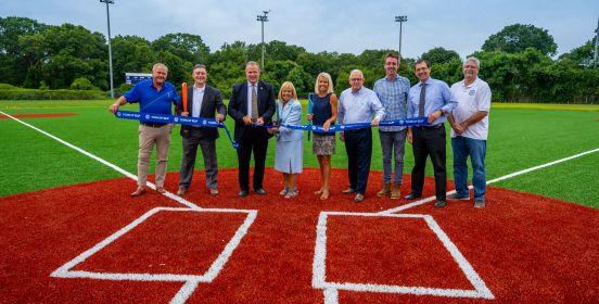 Supervisor Carpenter, Members of the Town Board, Pakrs Commissioner Owens and more gather infront of the batter boxes at home plate, with backs to new field and ribbon for cutting in their hands in side by side group photo.