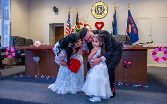 Newly wedded couple embrace young flower girl