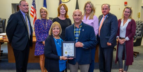 Islip Supervisor Angie Carpenter and the Islip Town Board stand beside Marian Guard Schoberl as he is presented the Town Certificate.