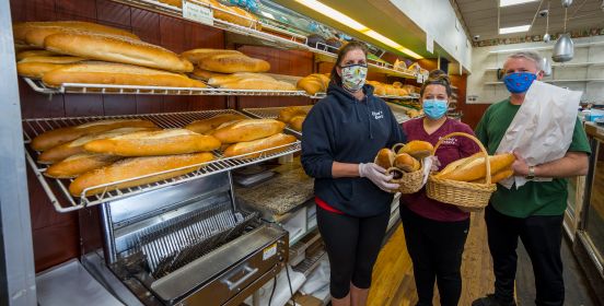 bakery members in masks hold bread in front of bakery wall