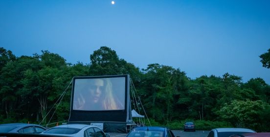 the moon shines glowing above the outdoor screen, with rows of cars lined up to view