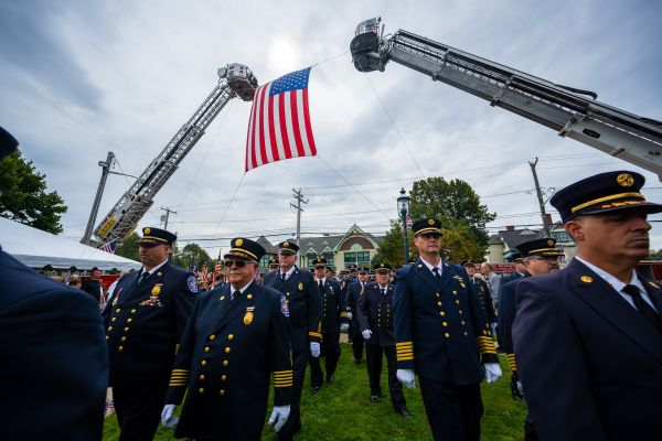 Local First Responders stand in formation underneath an American Flag surround the 9/11 Ceremony
