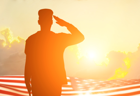 shadow of servicemember salutes into the sunset over an American flag