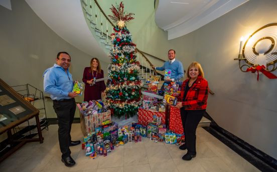 Supervisor Carpenter, YES Executive Director MaryAnn Pfeiffer and Galaxy Realty representatives in photo with toys under Christmas Tree
