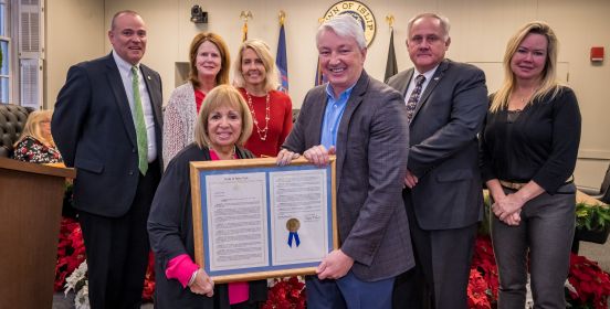 NY Senator Phil Boyle presents Town Supervisor Angie Carpenter with a resolution paying tribute to the town's growth to present day, as the Islip Town Board stands behind them for a photo.