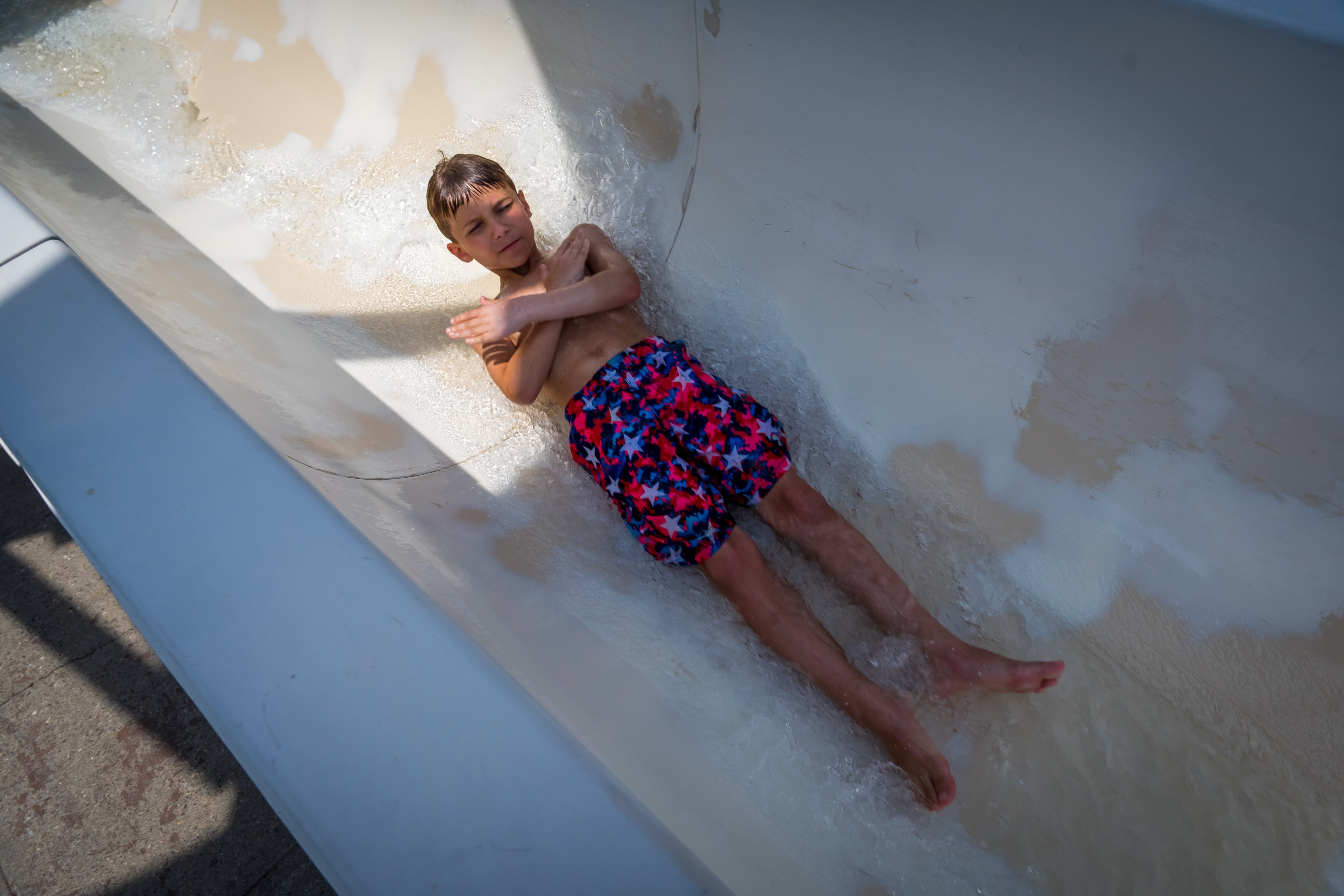 A boy mid water slide with arms crossed and rippled water rushing around him.