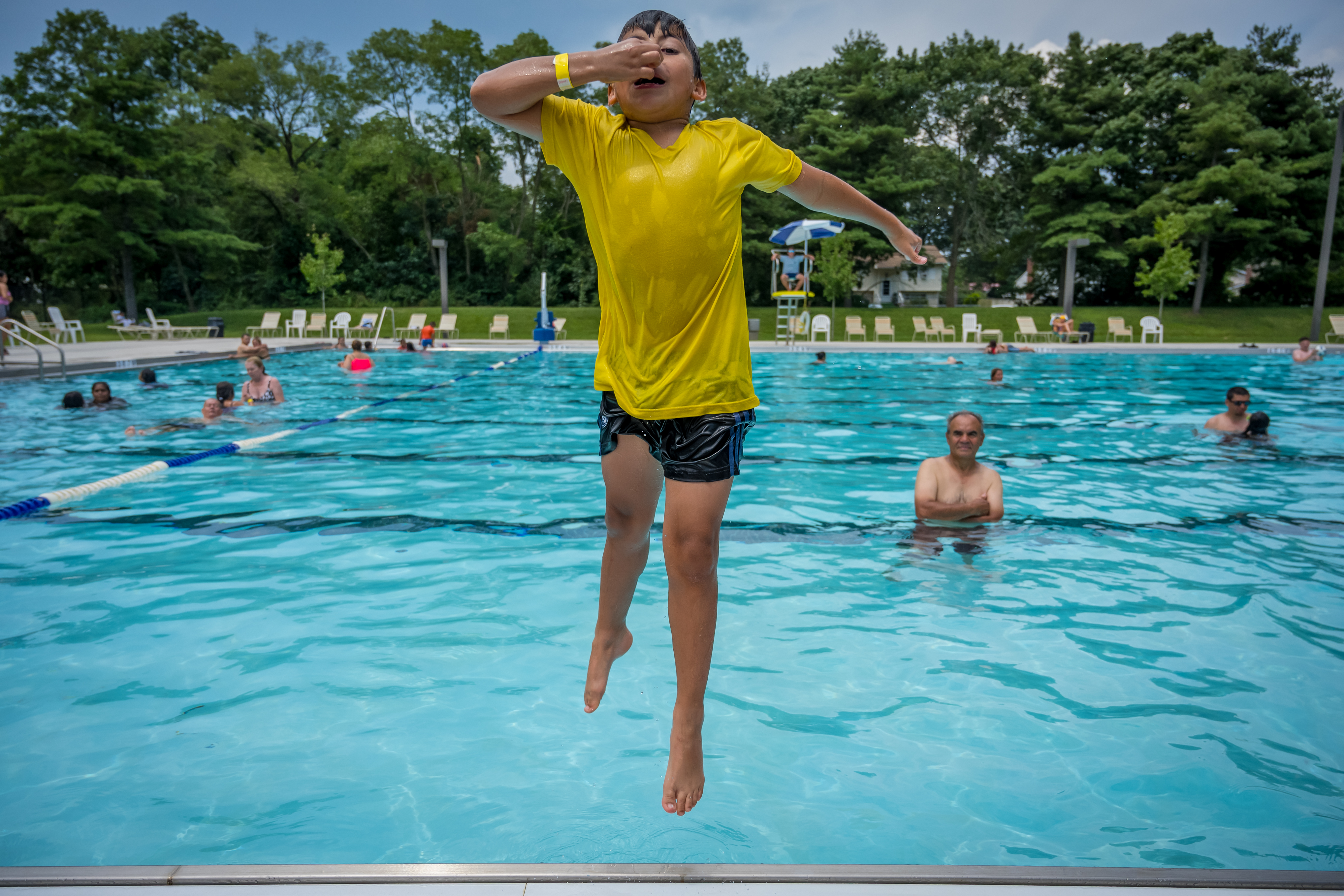 Boy in yellow shirt holds his nose as he jumps backwards into the new Roberto Clemente Pool