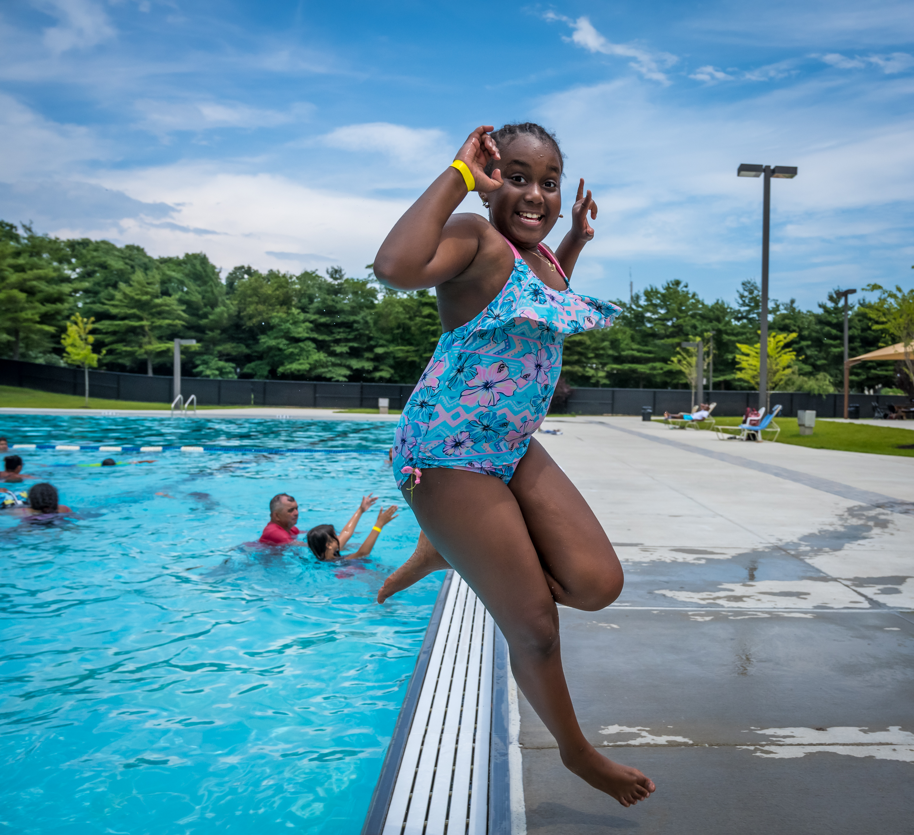 Girl smiles toward the camera as she leaps backwards into Roberto Clemente's new sparkling blue pool.