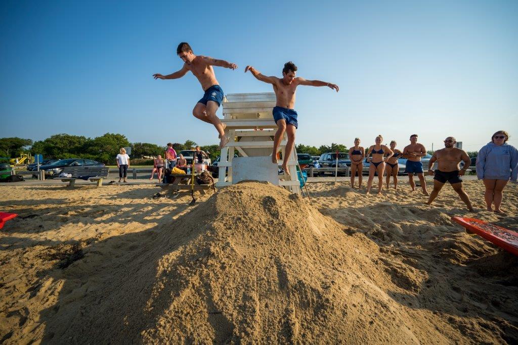 2 male lifeguards jump down from the lifeguard stand, leaping into action at the start of their timed run