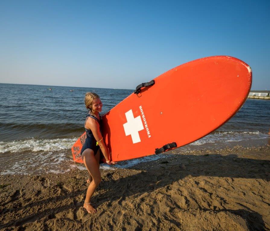 A female lifeguard smiles as she tows the red surfboard back to the starting zone.