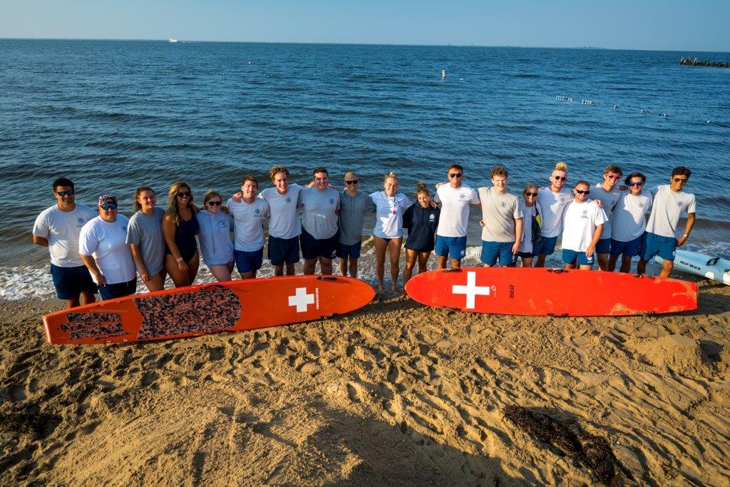 A group shot of all lifeguards with their backs to the water and surfboards at their feet