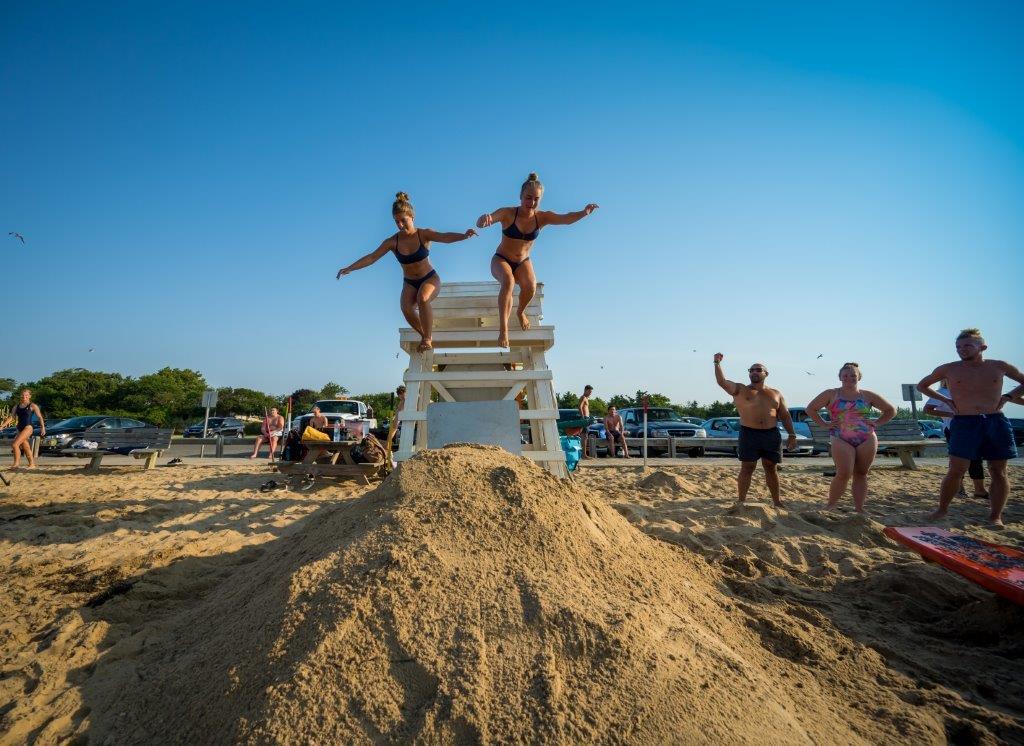 2 female lifeguards jump down from the lifeguard stand, leaping into action at the start of their timed run