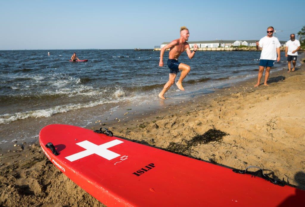 a male lifeguard reaches land in full sprinting motion as he continues his mad dash back to the starting zone